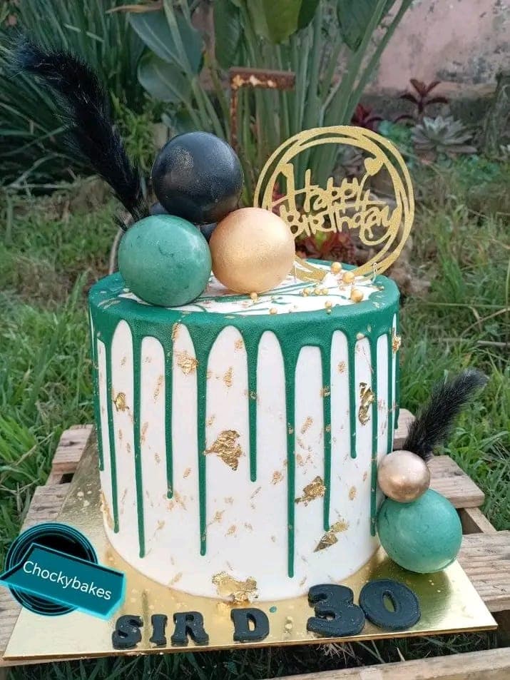 White birthday cake with green drip icing, gold leaf and chocolate spheres.