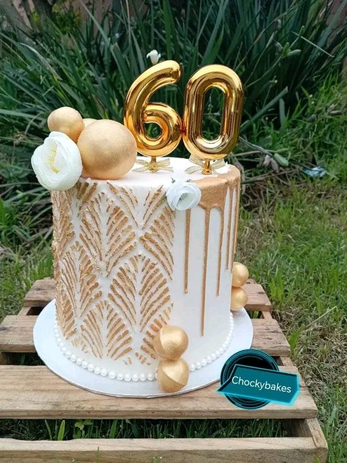 White and gold 60th birthday cake with textured gold leaves and white flowers.
