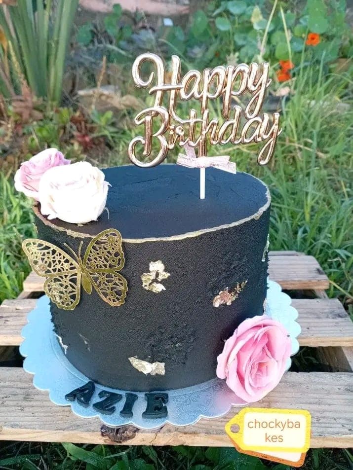 Black buttercream birthday cake with pink roses, gold leaf and a gold butterfly.