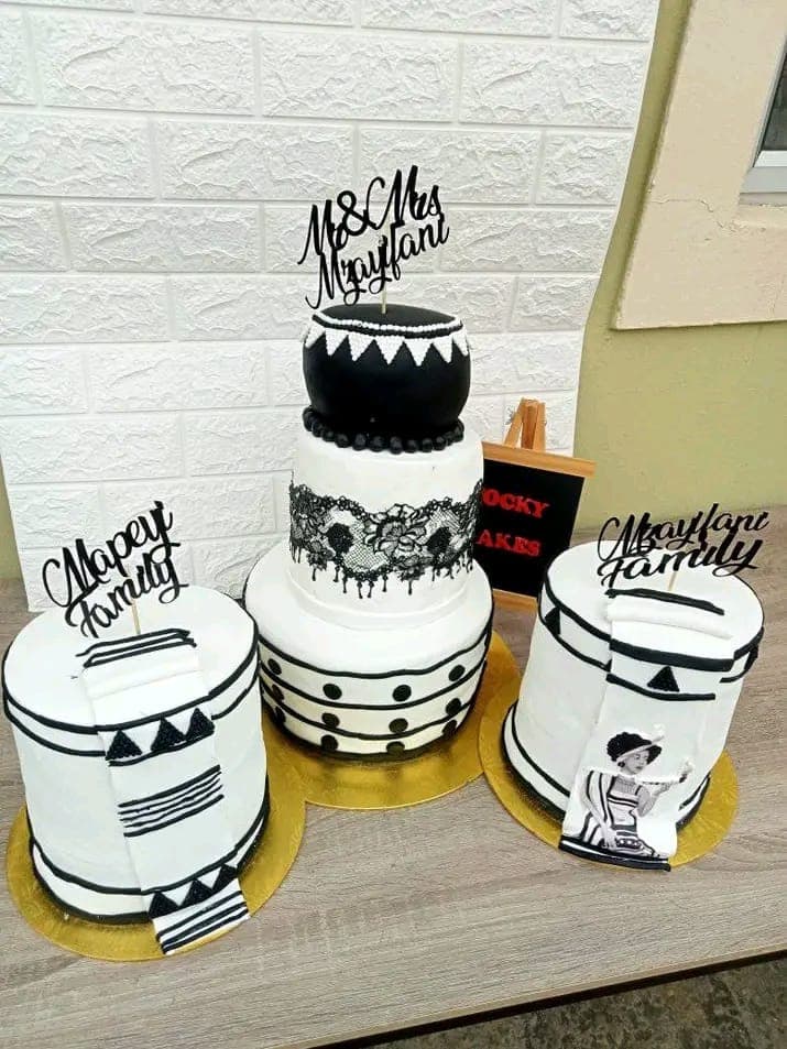 Three black-and-white celebration cakes with lace, geometric patterns and wedding toppers.